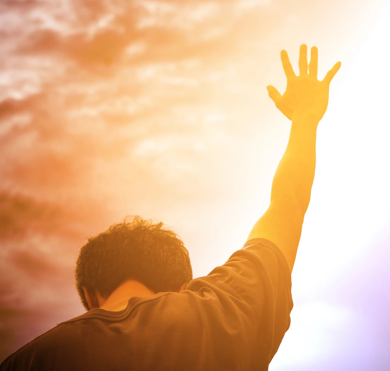 A young man raising his hand in worship at sunset