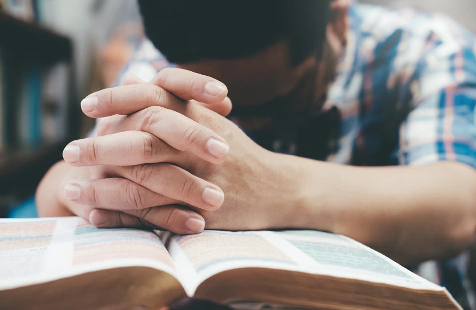 A student praying over an open Bible