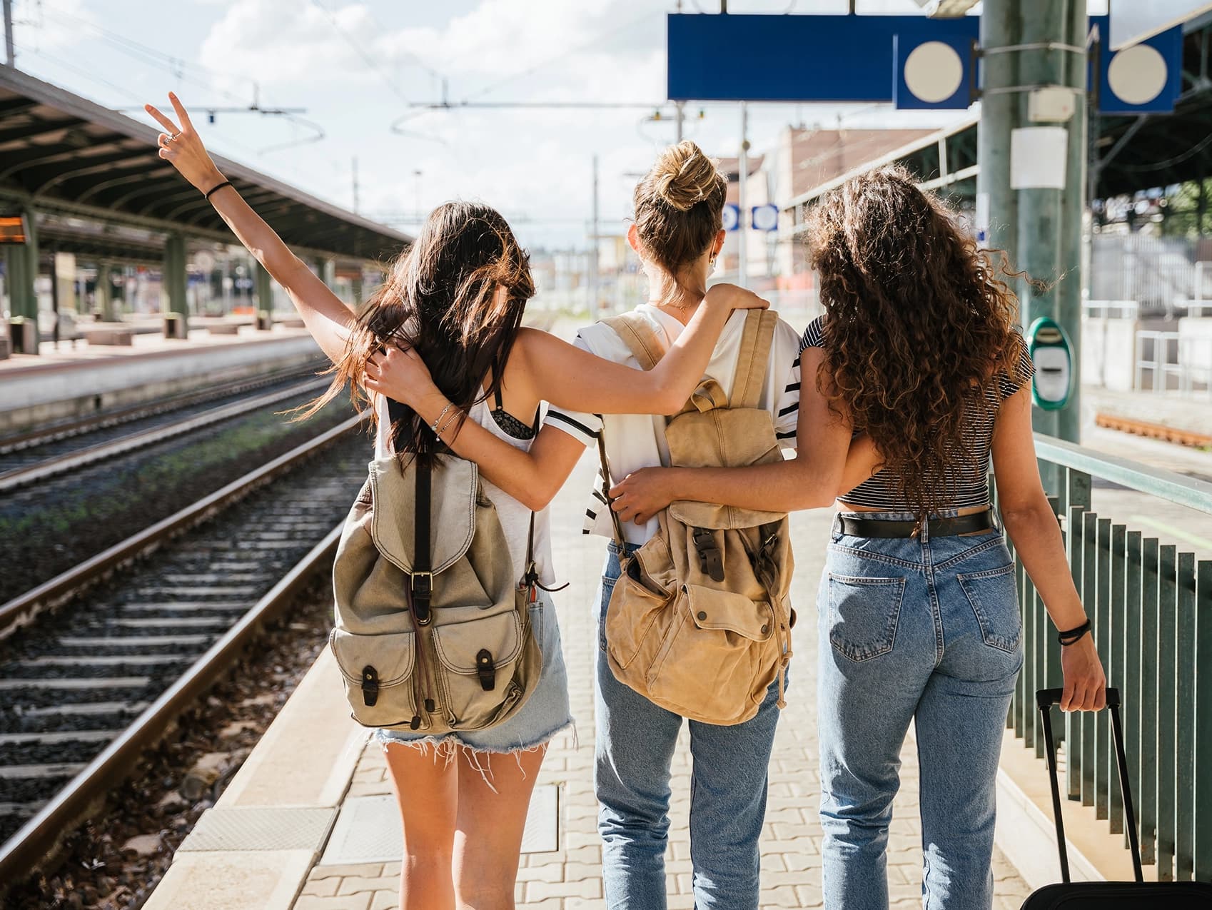 Three friends with backpacks setting off from a train platform