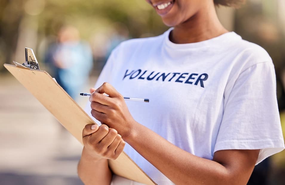 A volunteer wearing a "Volunteer" shirt writing on a clipboard